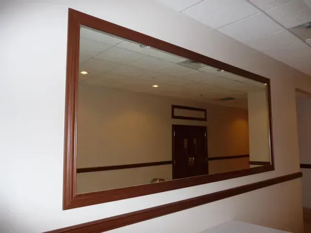 Large rectangular mirror with a dark brown frame mounted on a white wall in a hallway.