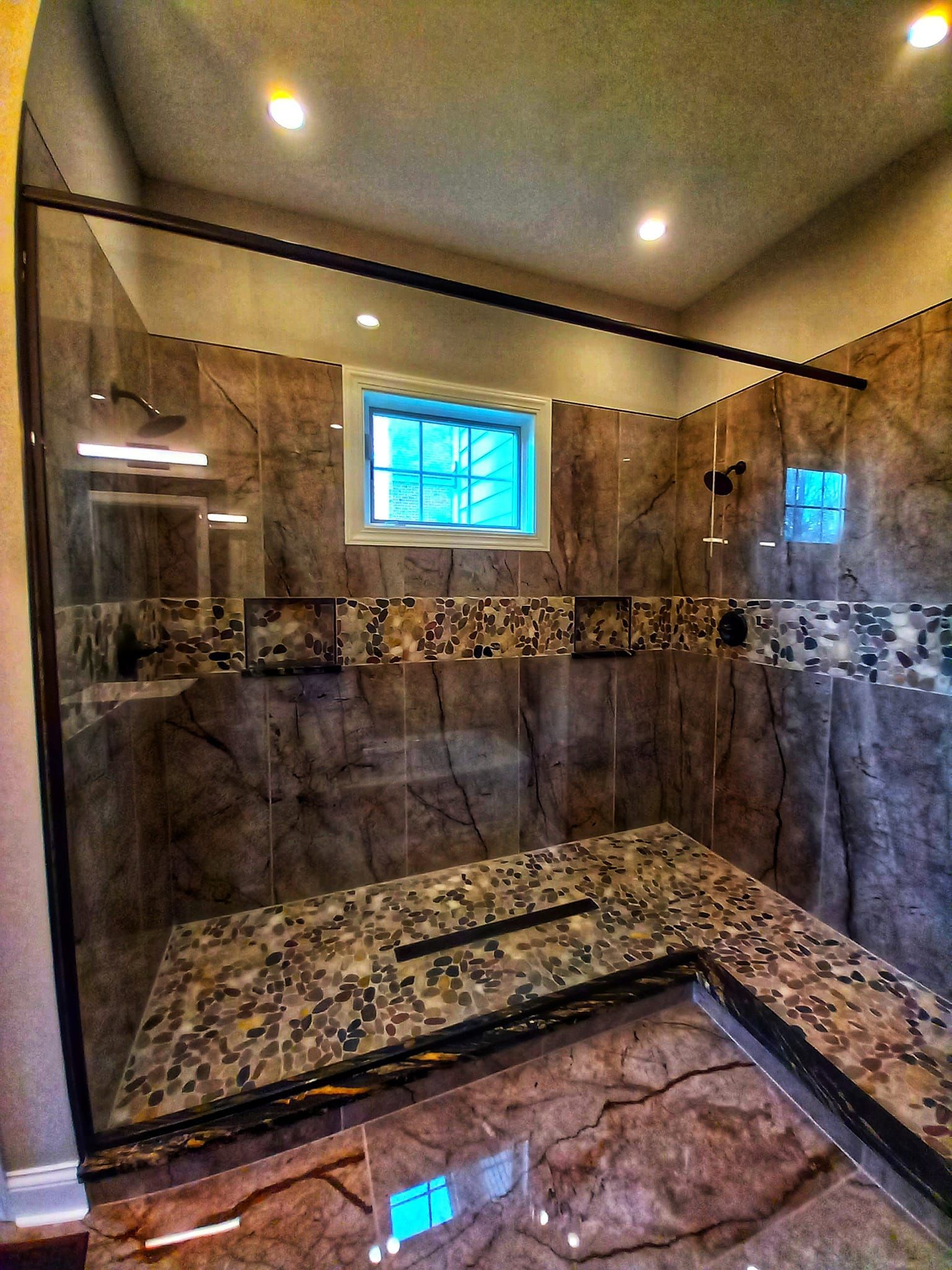 Glass-enclosed shower with granite bench, tile walls. Small window, recessed lighting.