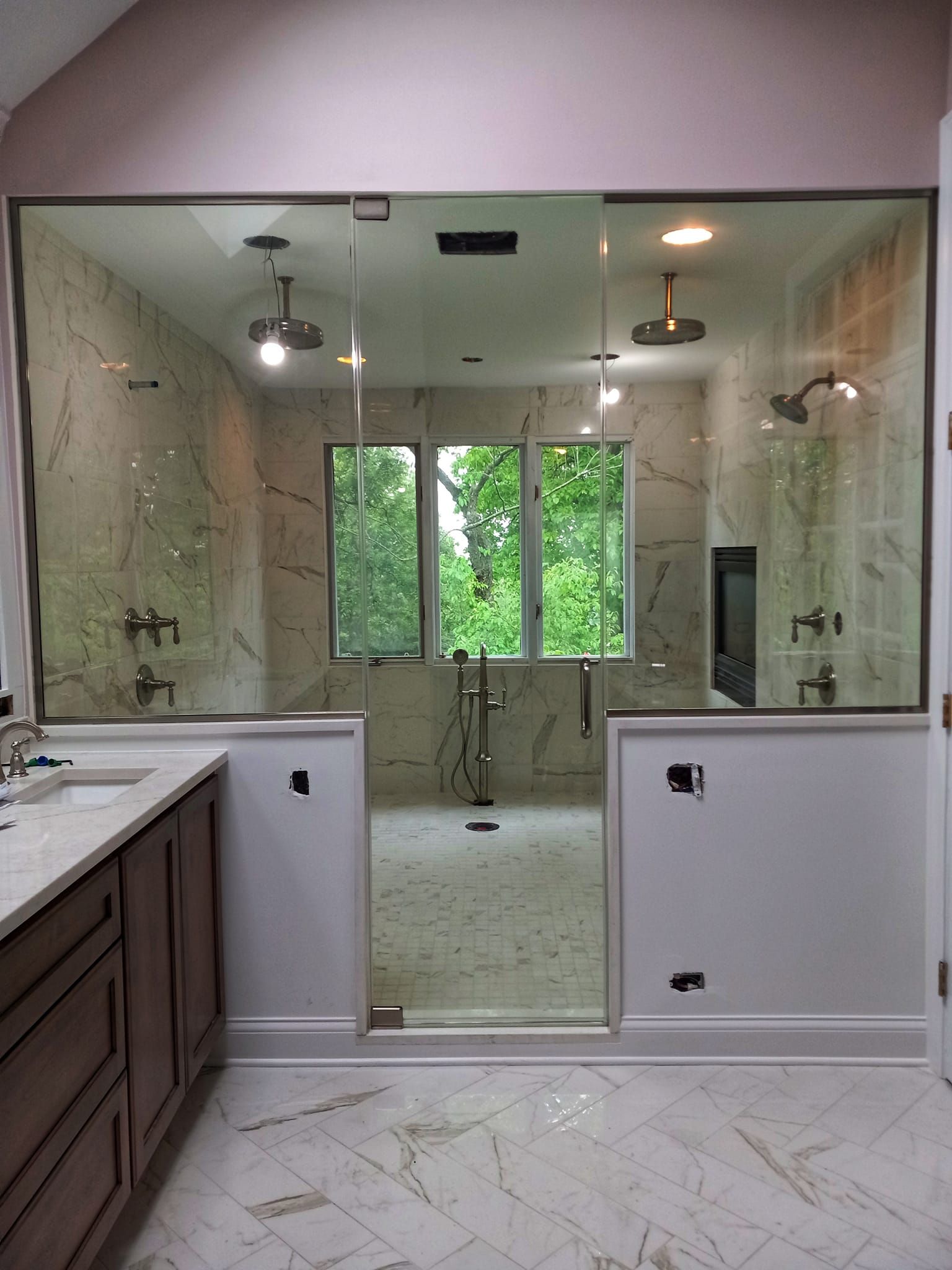 Bathroom with glass shower, marble tile, vanity, and windows overlooking greenery.