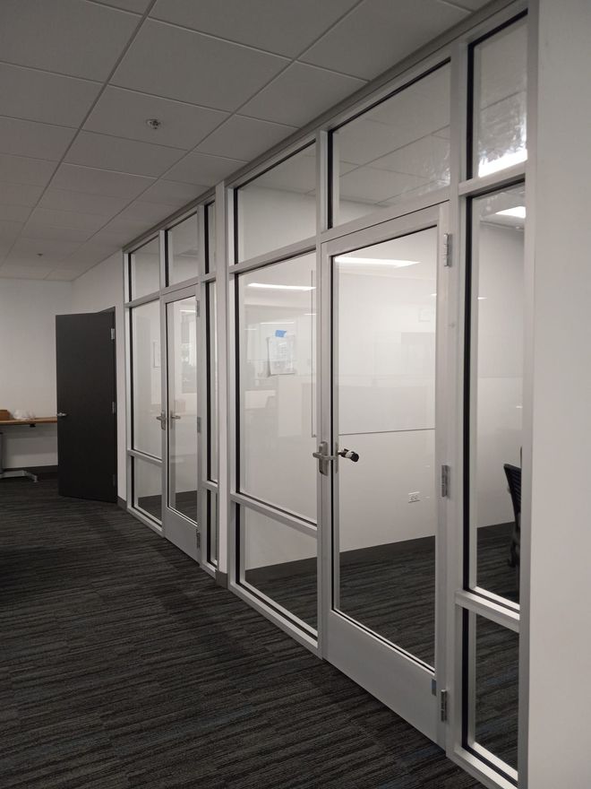 Hallway with glass-walled offices and gray carpet. White walls and ceiling.