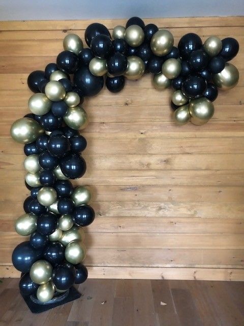 a bunch of black and gold balloons on a wooden wall