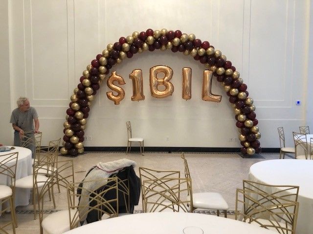 a room with tables and chairs and a balloon arch that says $ 1bil