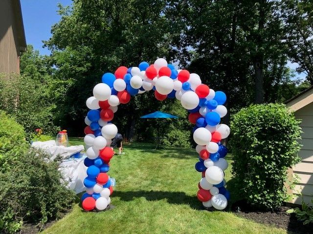 a red , white and blue balloon arch in a yard .