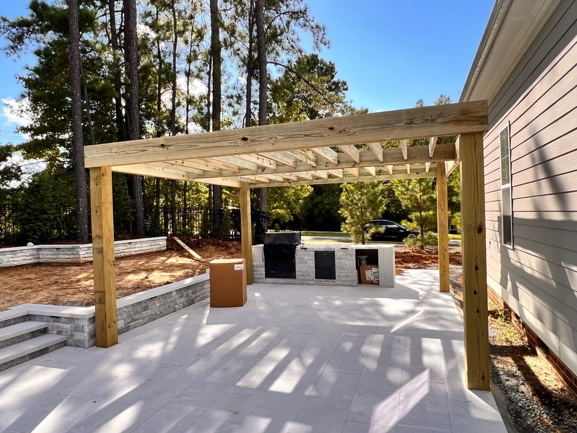 outdoor kitchen with a pergola, on a gray concrete patio, with a stone accent wall