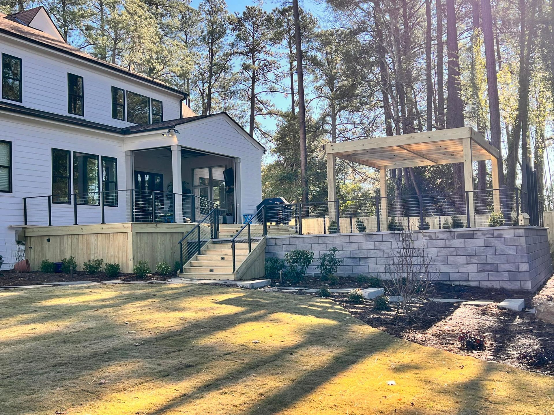 backyard with a two-story white house, wooden deck, patio with pergola, and low stone wall