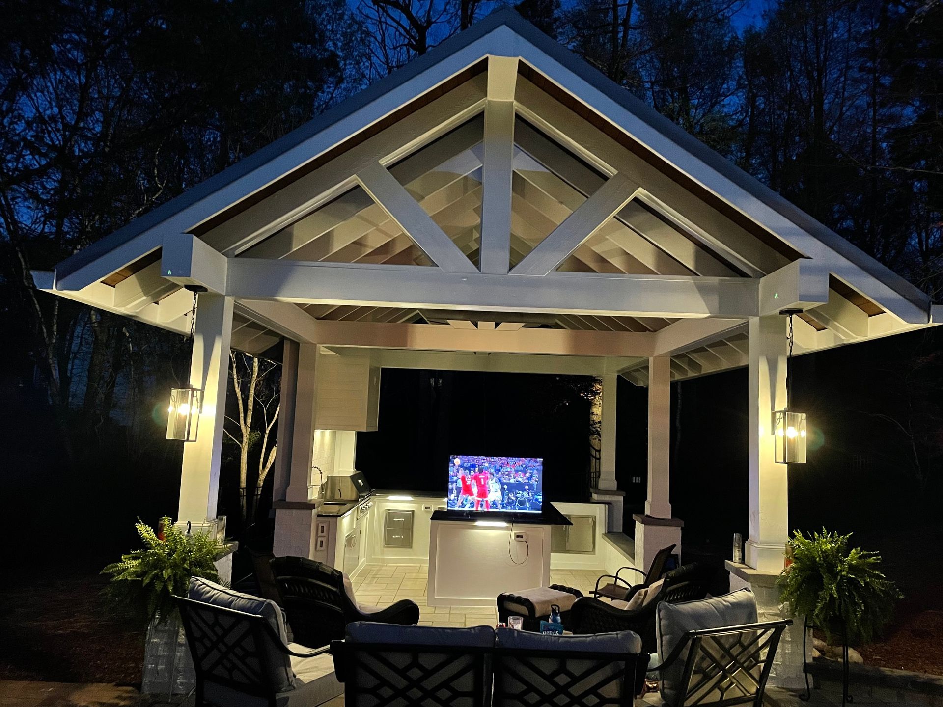 outdoor pavilion with lights, TV, seating, and a built-in kitchen at night