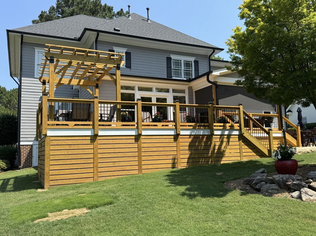 a wooden deck with a pergola is attached to a gray two-story house