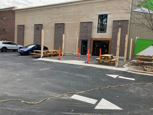 Exterior of a building with picnic tables, temporary wooden posts, and parking lot arrows.