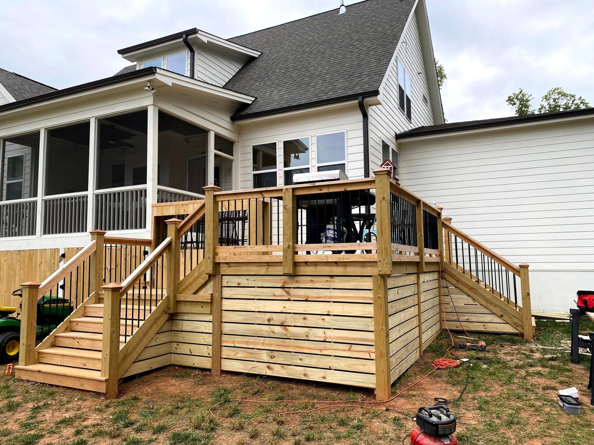 a wooden deck with stairs, black railings, and a screened porch attached to a white house