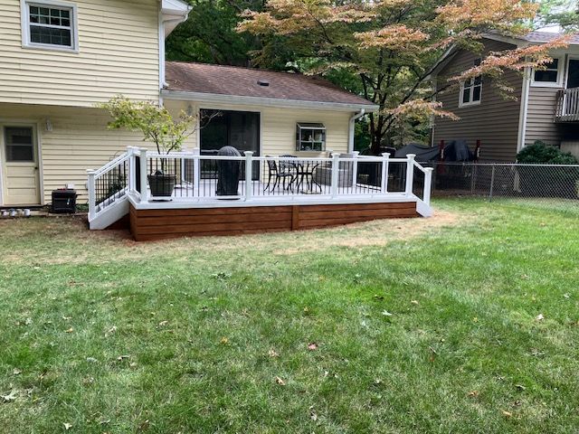 a wooden deck with white railings and a brown base, attached to a yellow house