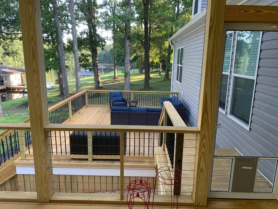 a screened porch with deck and lake view; blue outdoor furniture, grill, and trees in the background