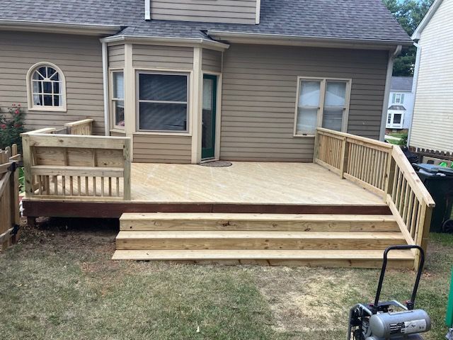wooden deck with steps and railings attached to a beige house, surrounded by grass and a small fence
