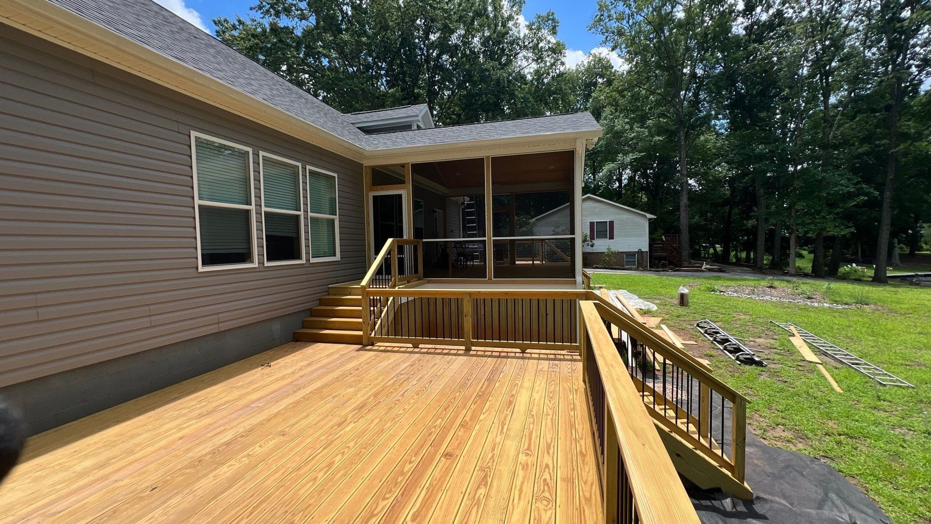 a wooden deck with screened porch, brown siding, and lush green yard under blue sky