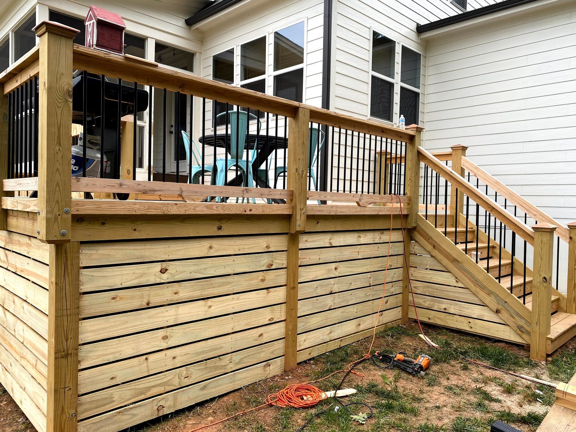 a wooden deck with black railing, steps, and horizontal siding against a white house