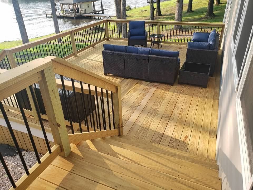 a wooden deck with black railing and blue outdoor furniture, overlooking a lake