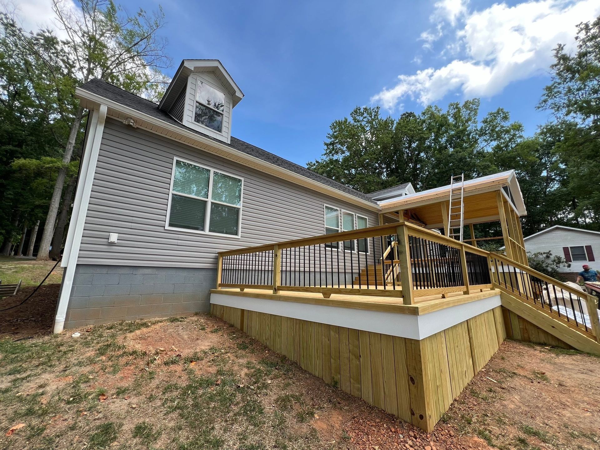 a house with gray siding, a new wooden deck, and a dormer under a blue sky