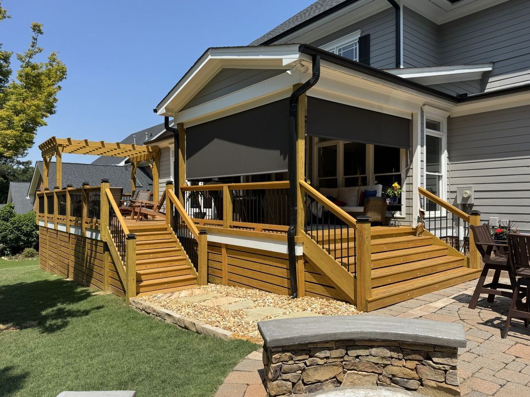 wooden deck with steps and black sun shade; next to a house with light siding