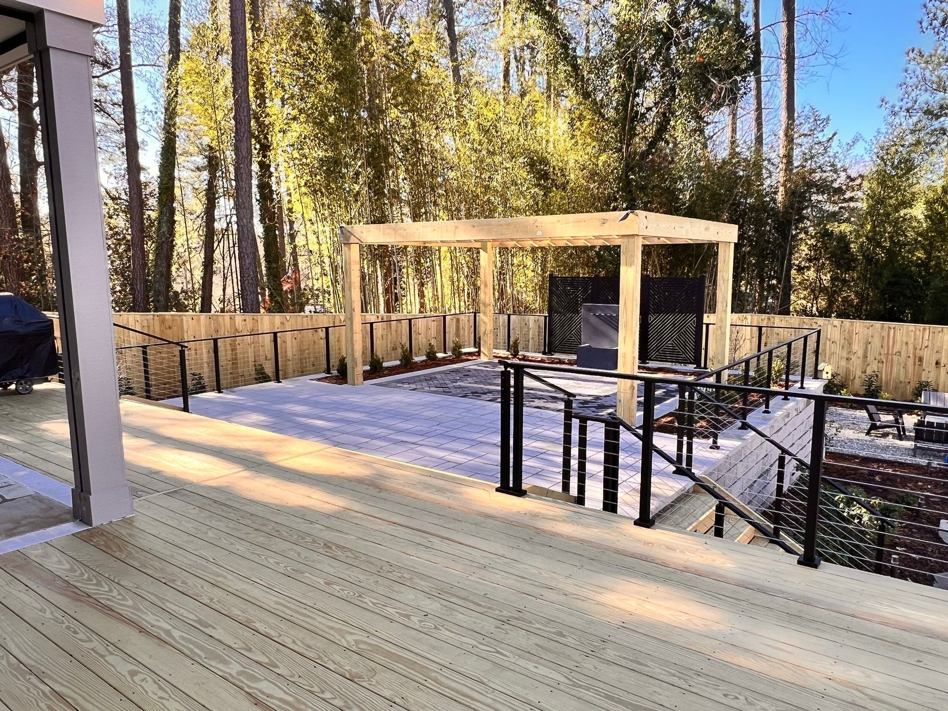 A wooden deck with a pergola and stairs leading to it surrounded by trees