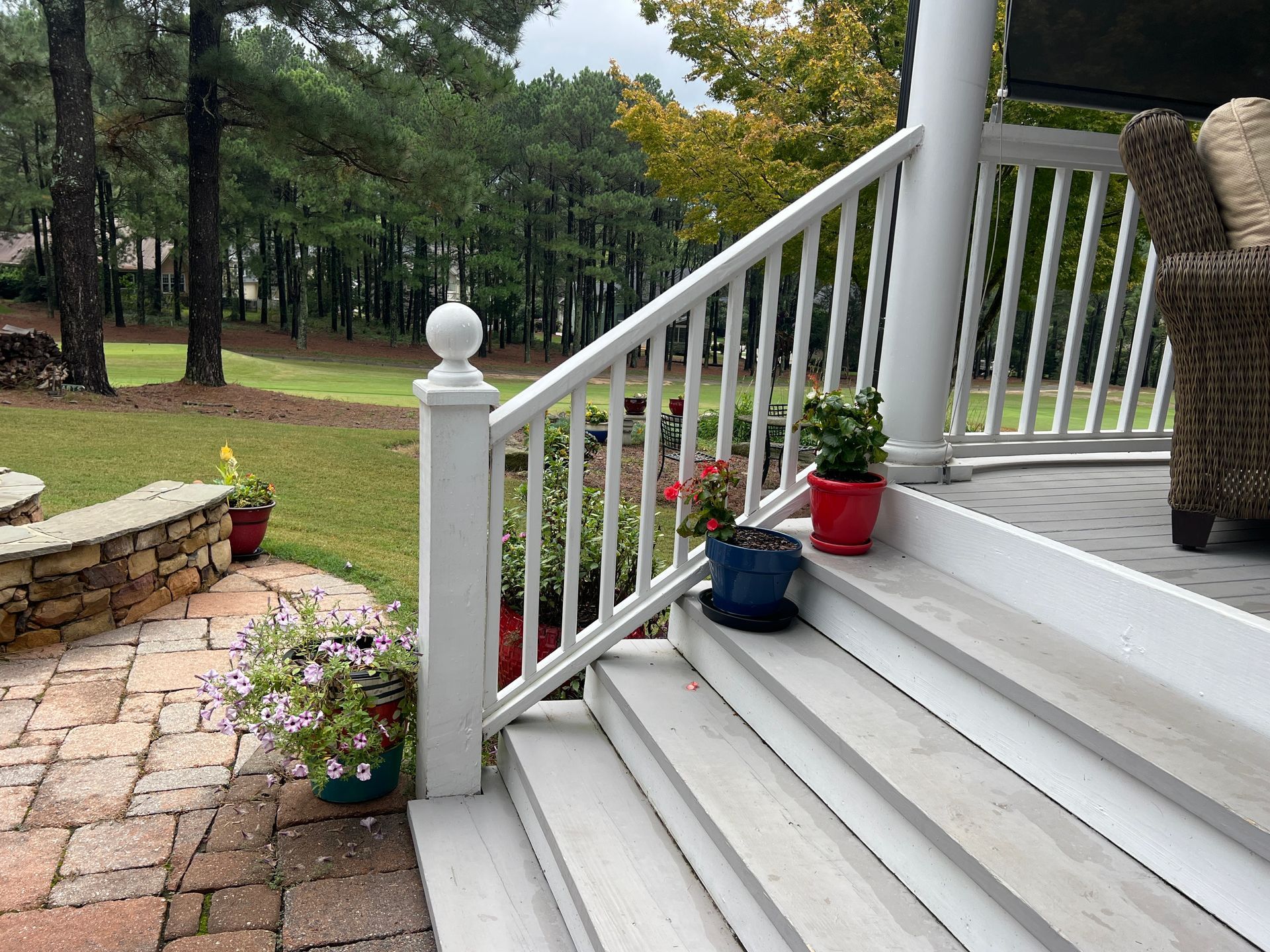 A white railing on a porch with potted plants on the steps