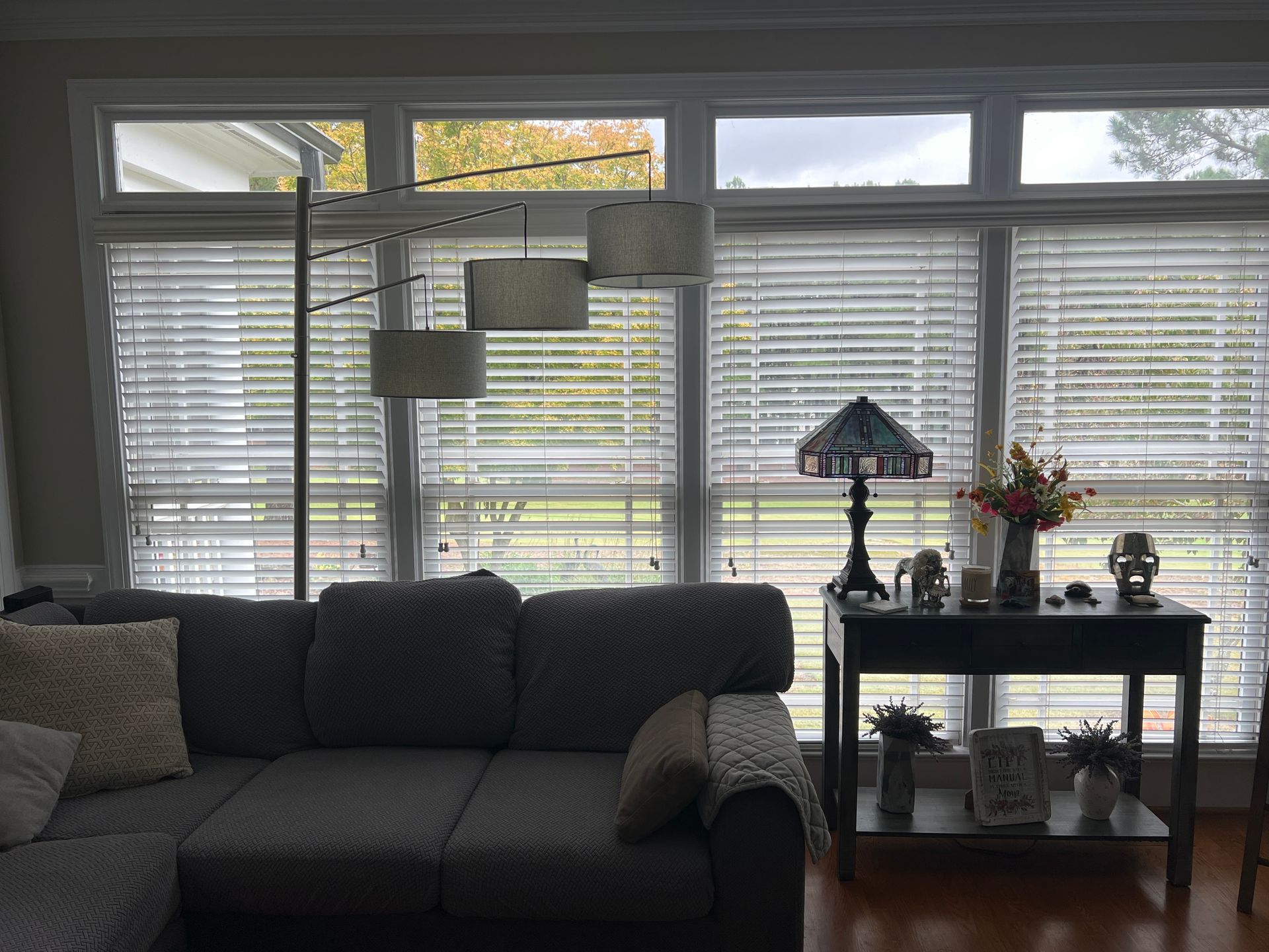 A living room with a couch, table, lamp and blinds.