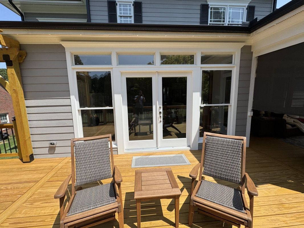 a wooden deck with two chairs and small table in front of French doors