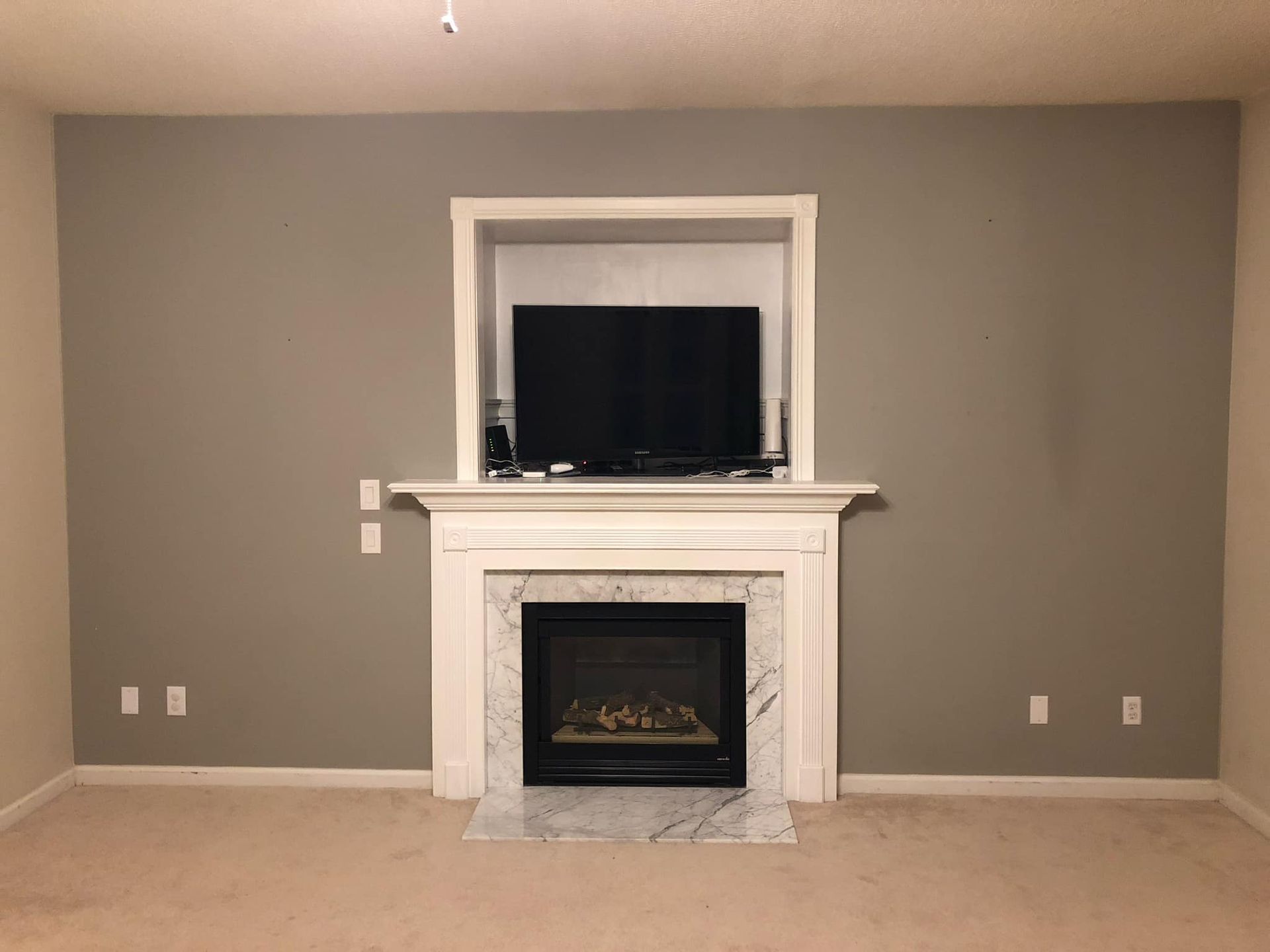 A fireplace with TV mounted above it on a gray wall, beige carpet, white mantel, and white trim around the TV
