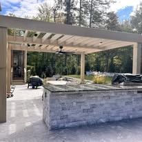 A large outdoor kitchen with a pergola and a grill.