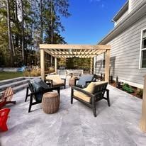 A patio with a pergola and chairs in front of a house.