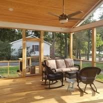A screened in porch with a couch , rocking chairs , and a ceiling fan.