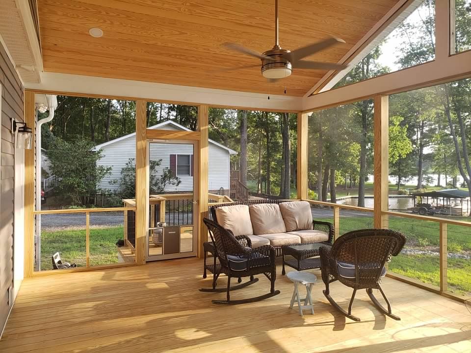screened porch with light wood ceiling and flooring, furnished with seating overlooking a lake