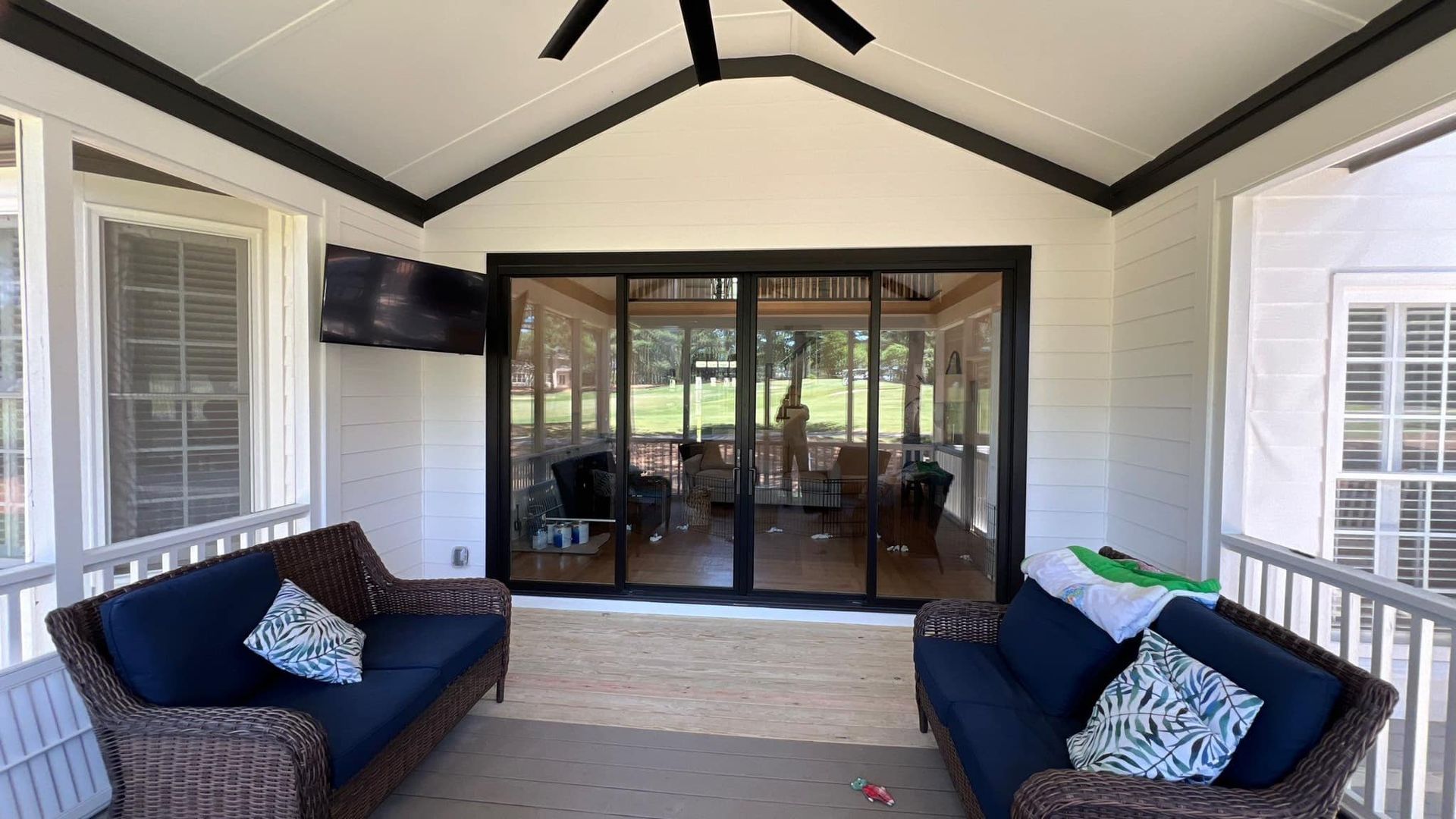 screened-in porch with couches, TV, and sliding glass doors overlooking a yard; black and white color scheme