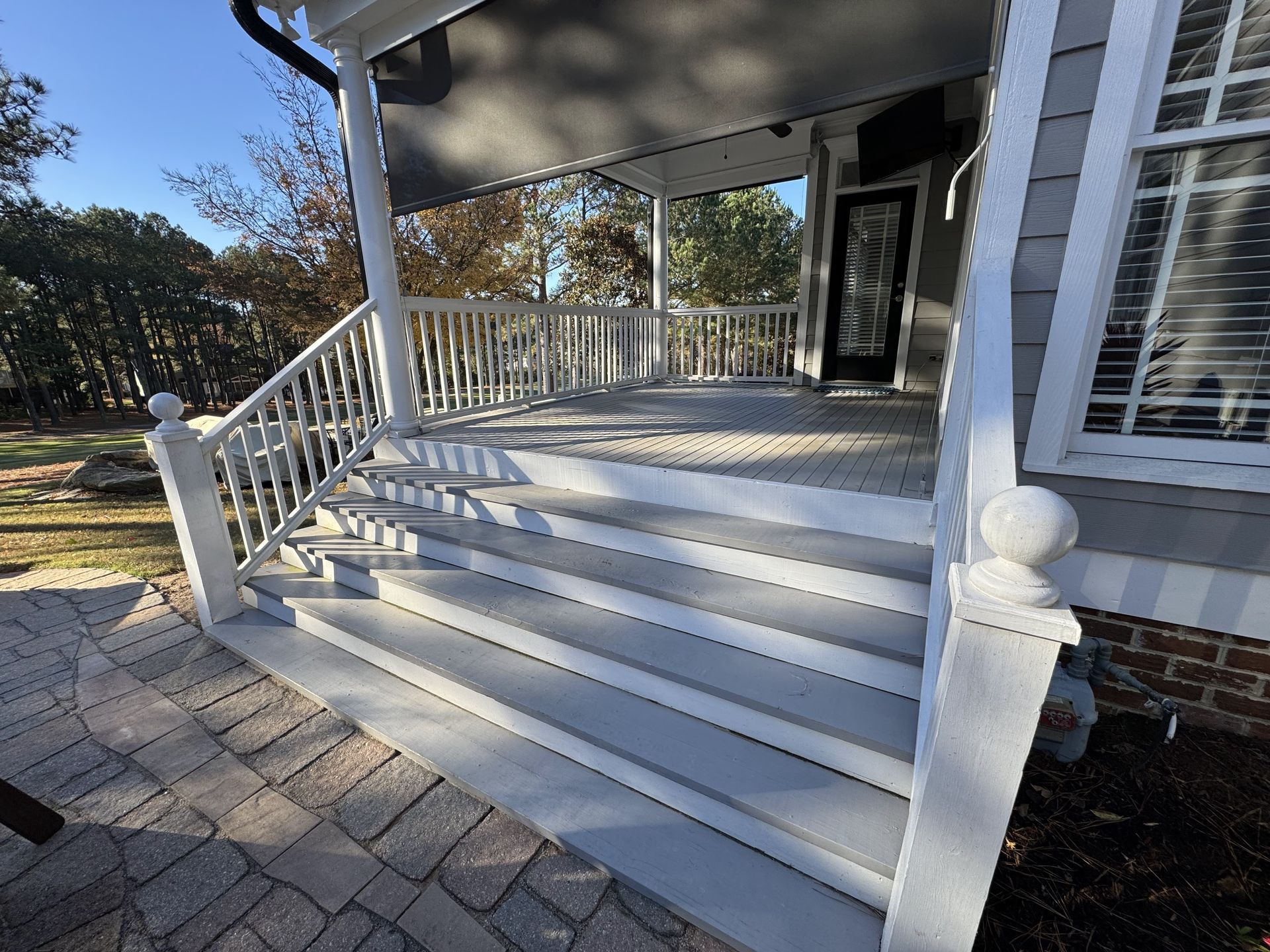 gray porch with steps, white railing, and a door, sunny day