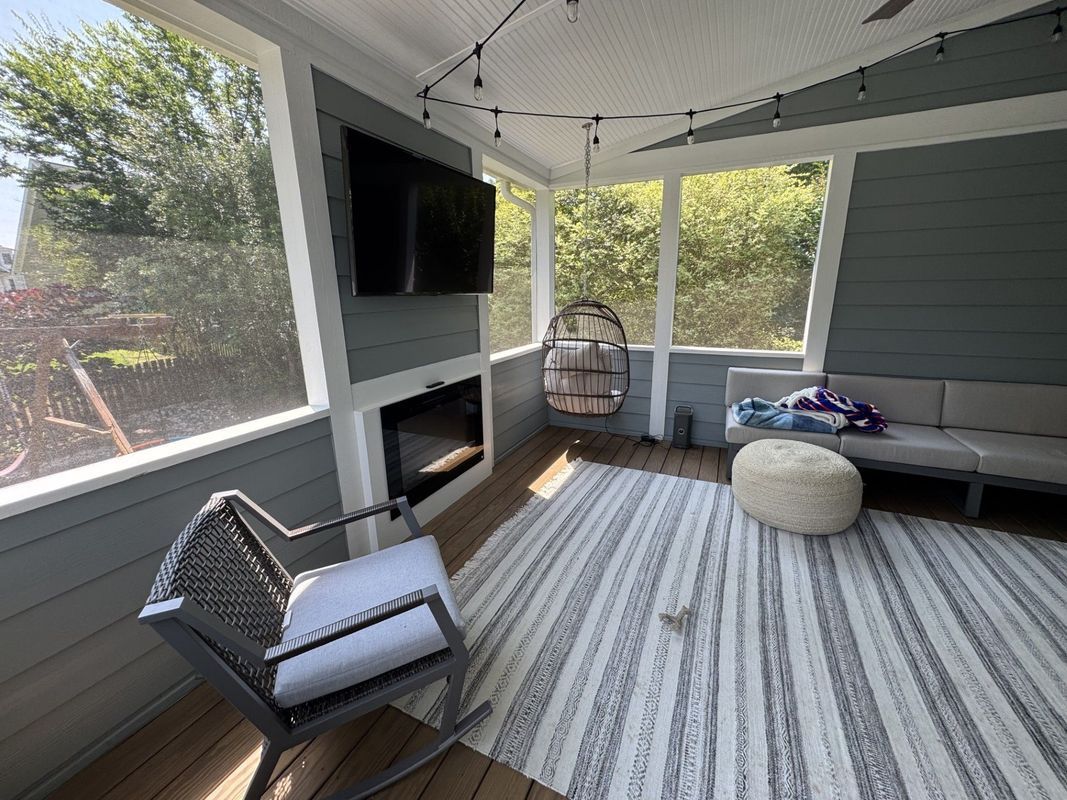 screened-in porch with TV, fireplace, seating, rug, and hanging birdcage, overlooking trees
