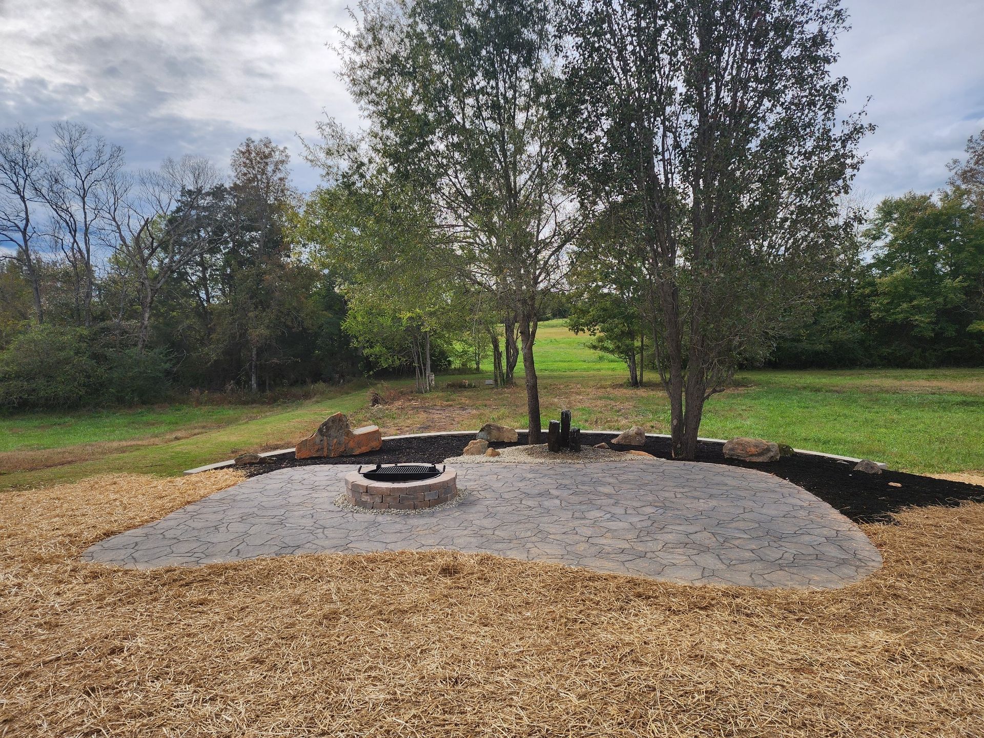 A fire pit in the middle of a field with trees in the background.