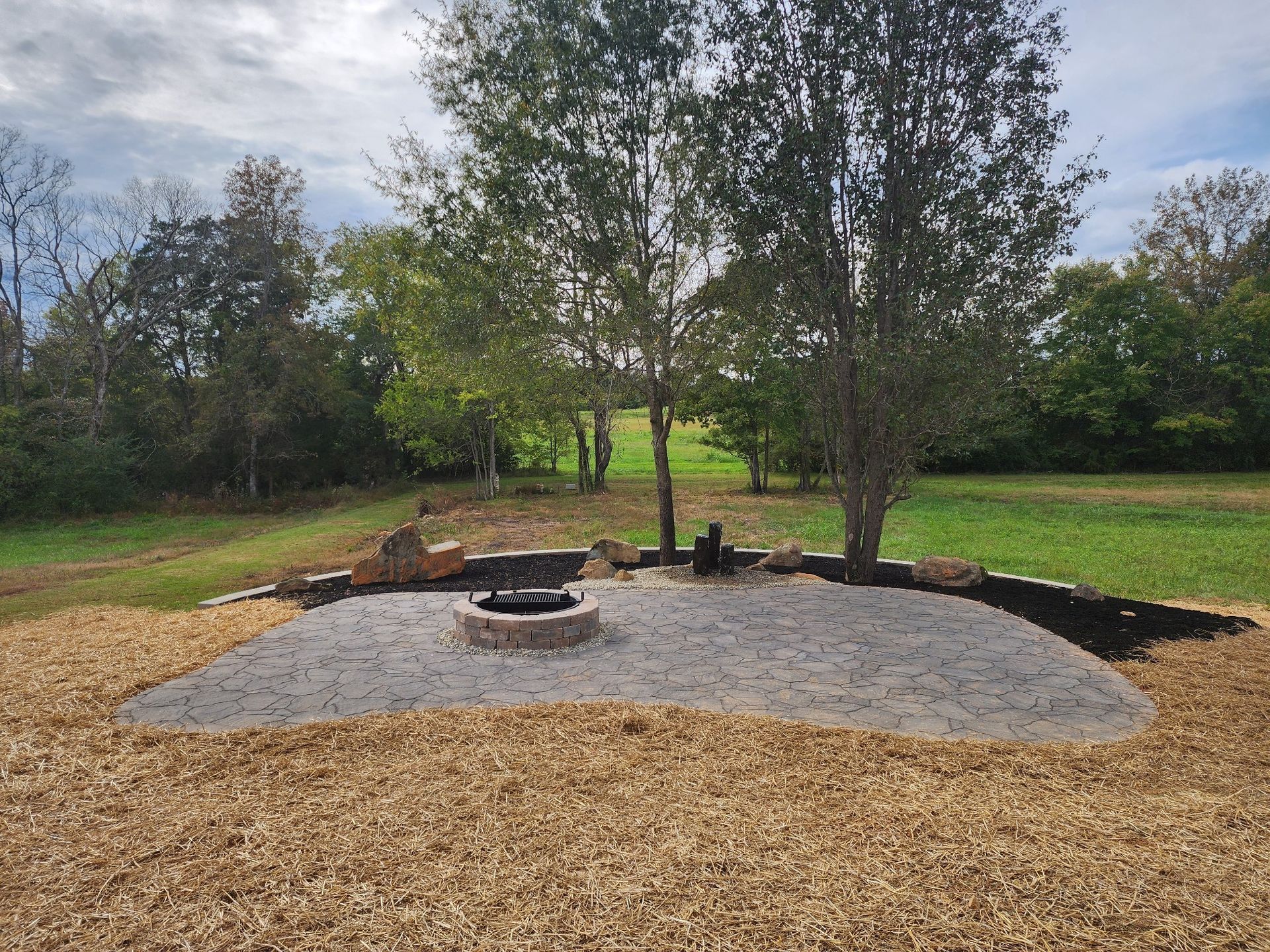 A fire pit in the middle of a field with trees in the background.