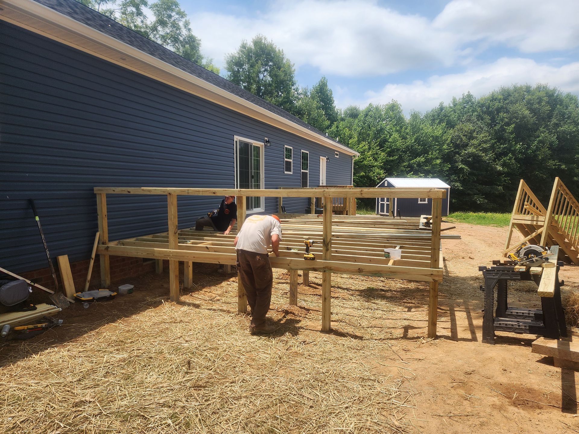 A man is working on a wooden deck in front of a house.
