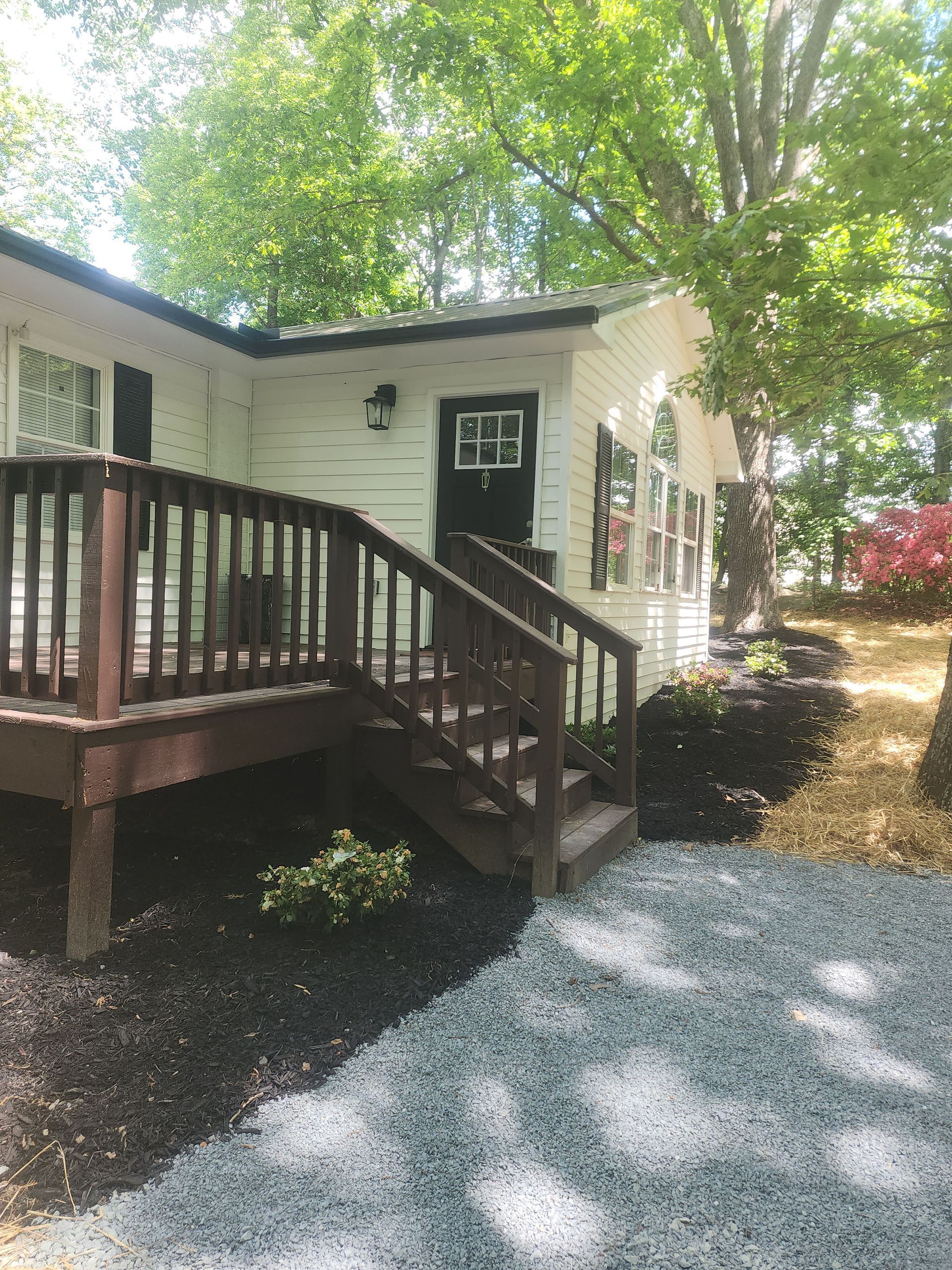 A white house with a wooden deck and stairs leading up to it.