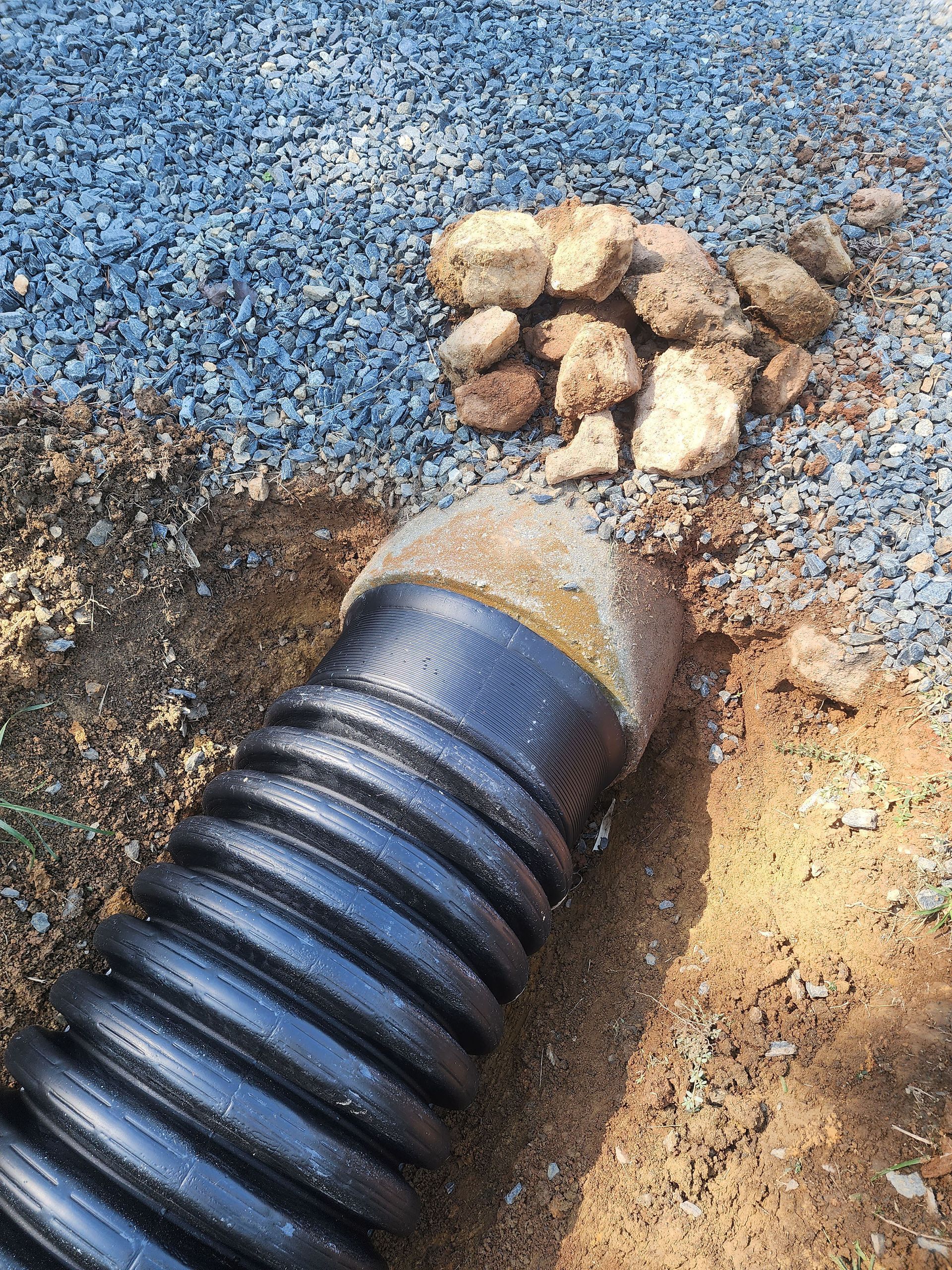 A black pipe is sitting in the dirt next to a pile of rocks.