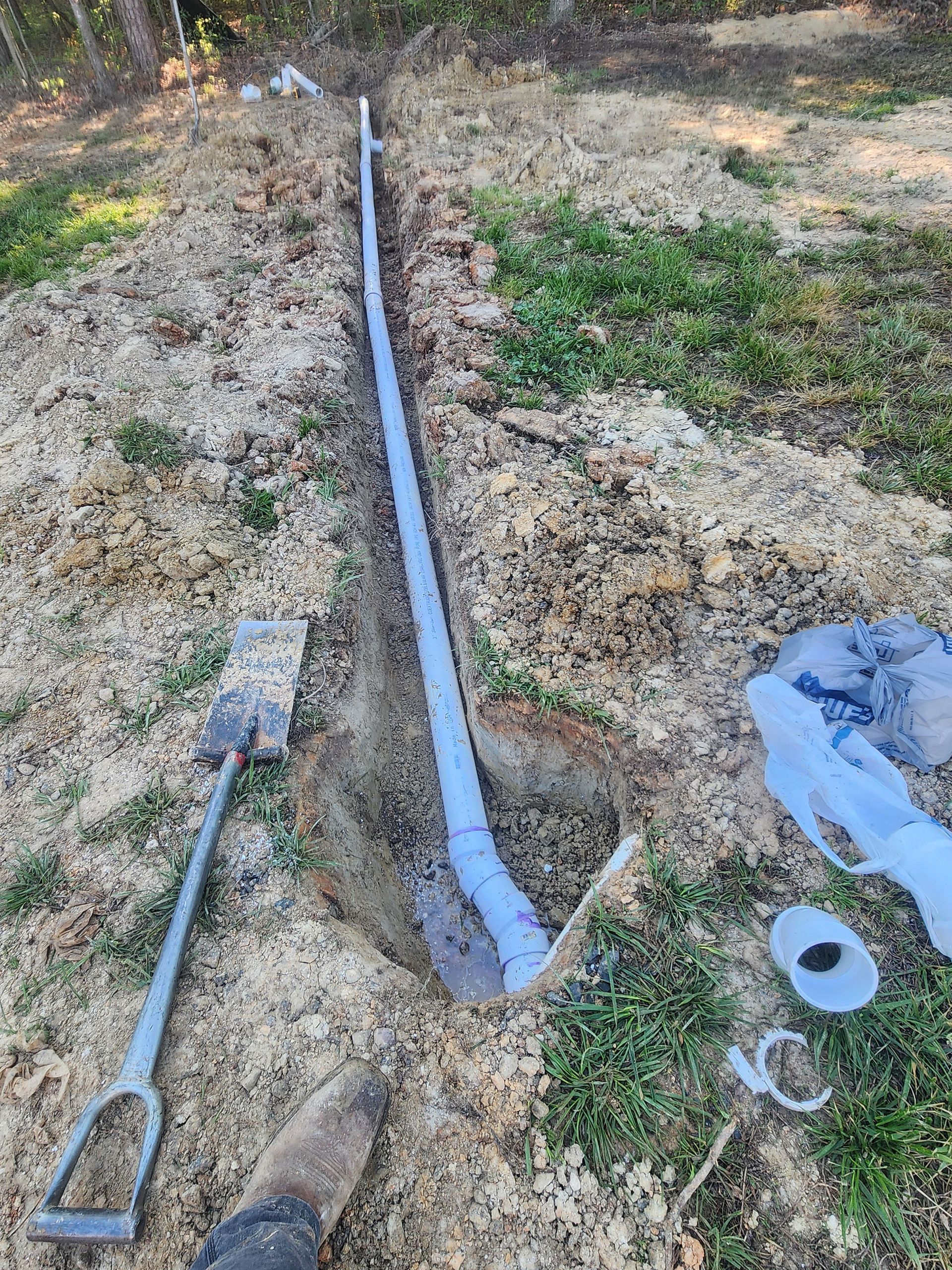 A pipe is being installed in the ground next to a shovel and tape.
