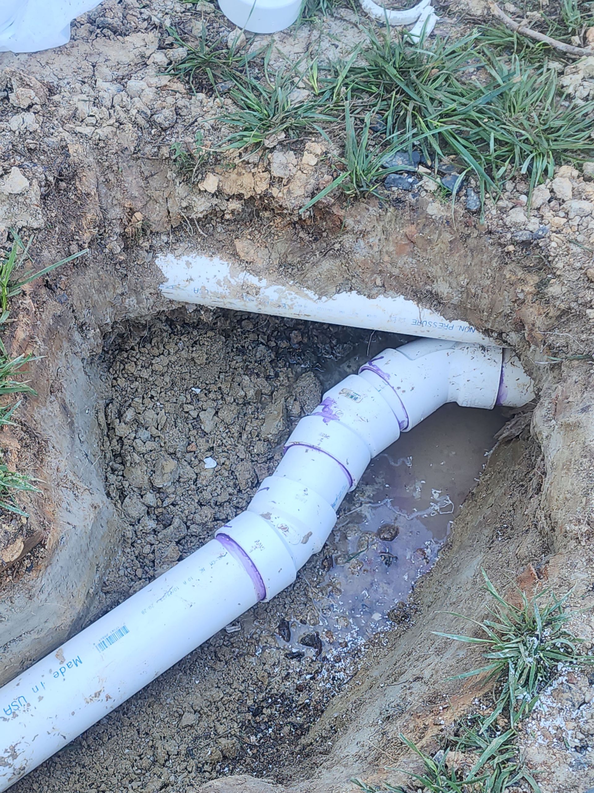 A white pipe is coming out of a hole in the ground.