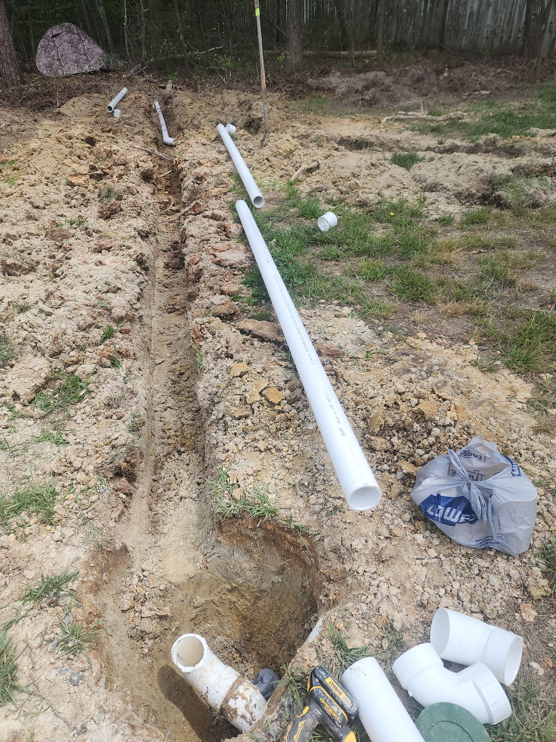 A bunch of pipes are laying on the ground in a hole.