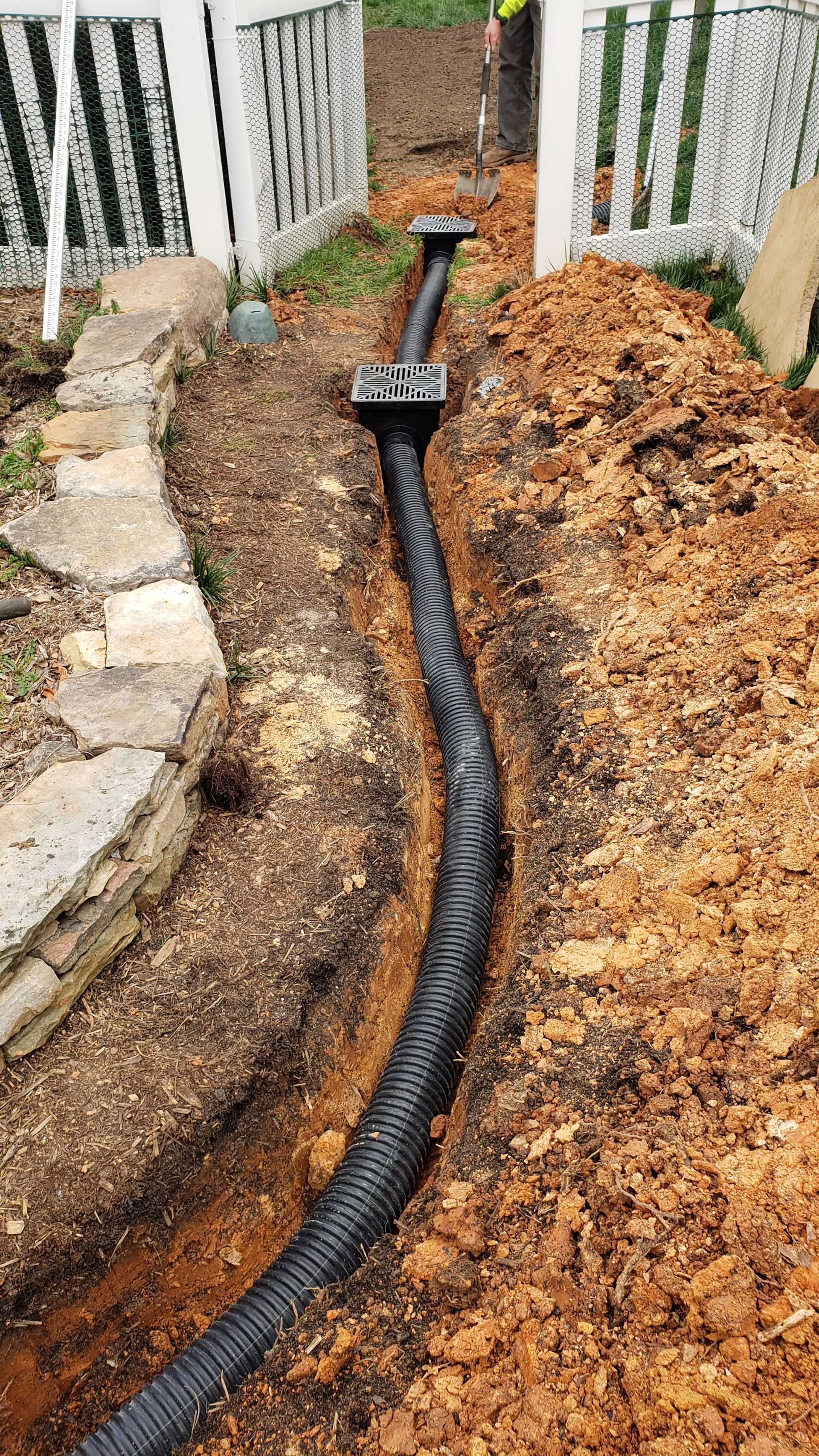 A drain pipe is being installed in the dirt next to a stone walkway.