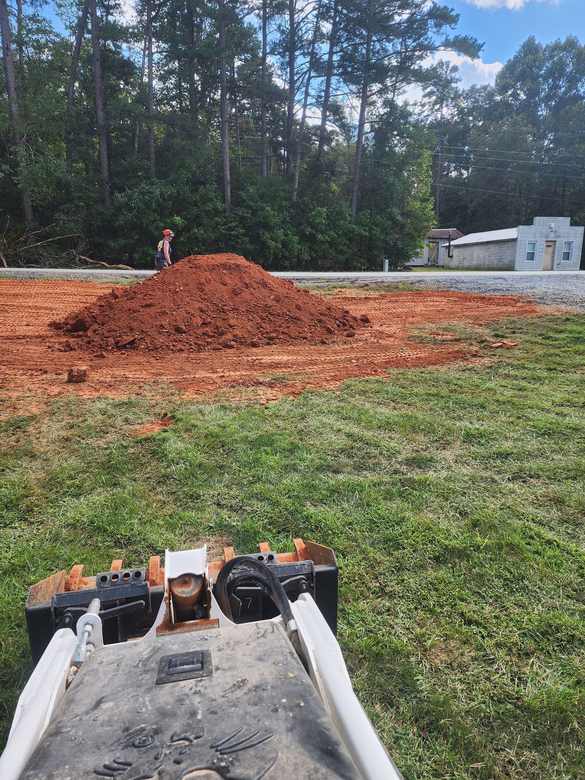 A person is standing in a field with a pile of dirt in the background.