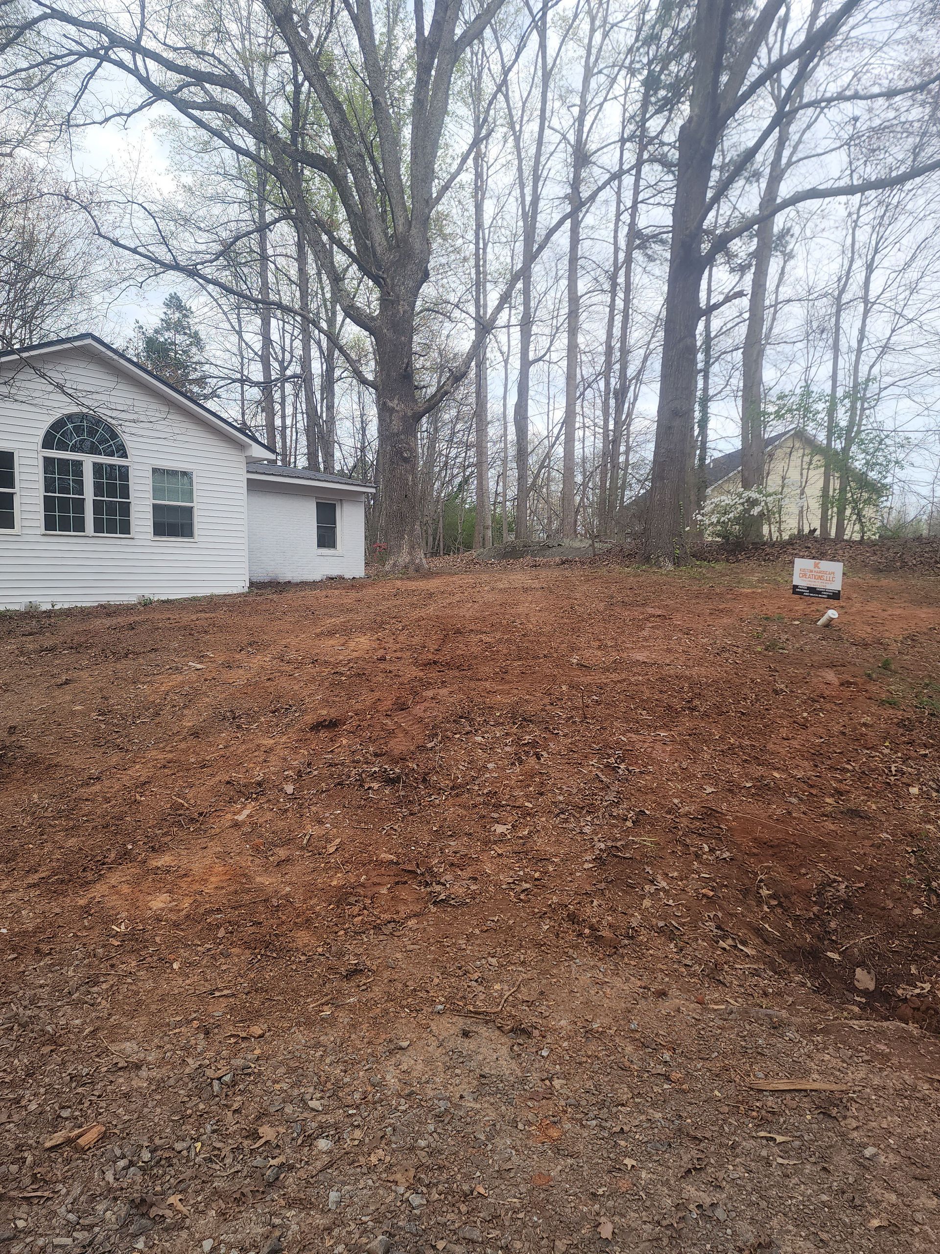 A white house is sitting on top of a dirt field surrounded by trees.