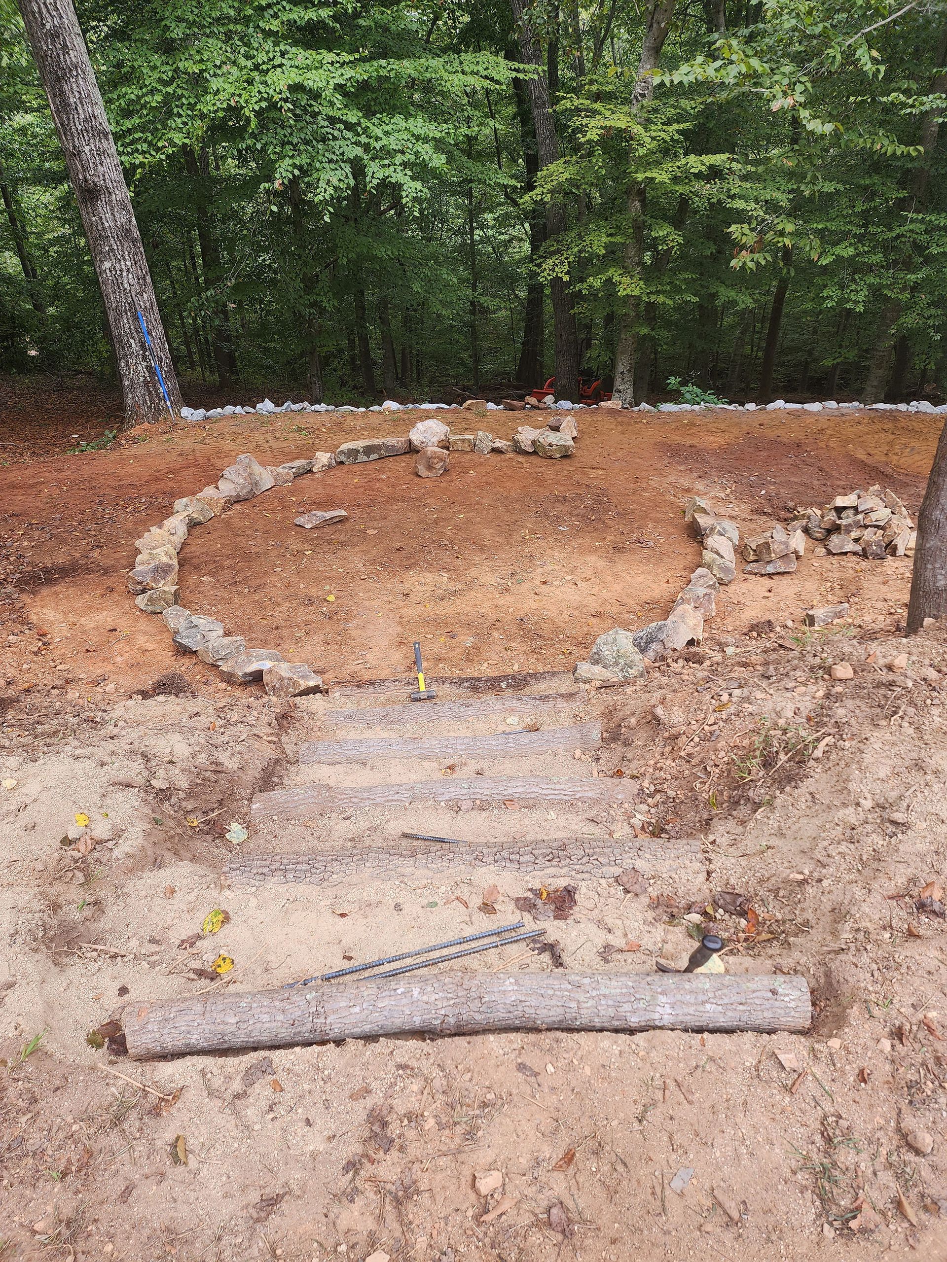 A circle of rocks and steps in the middle of a dirt field in the woods.