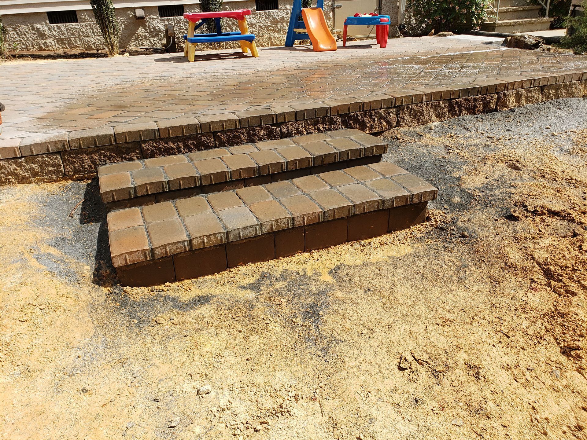 A set of steps leading up to a patio with a slide in the background.