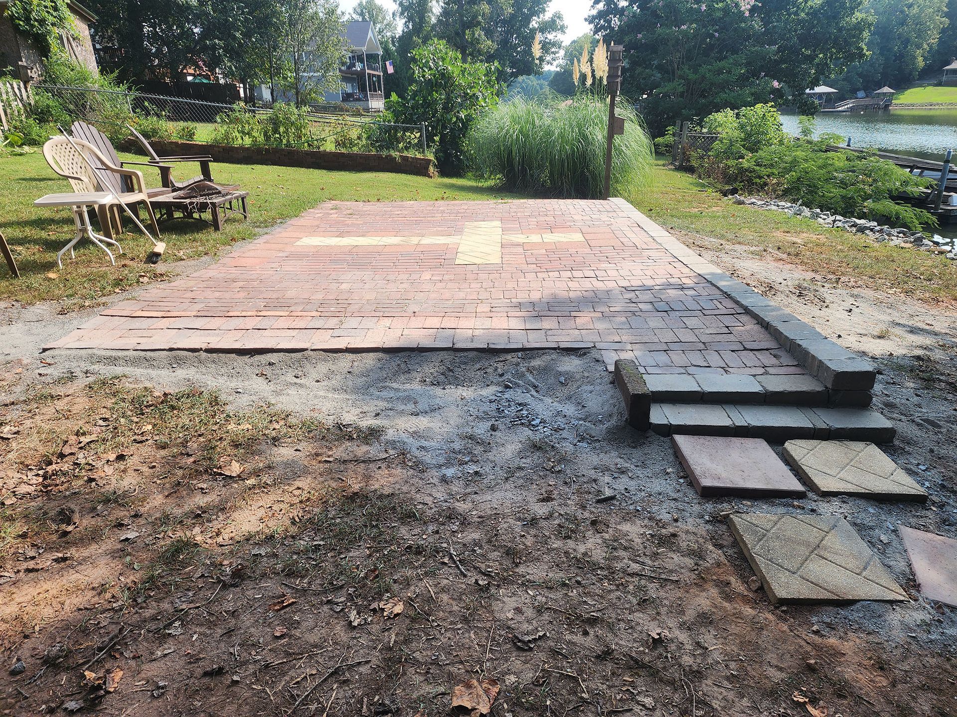 A brick patio is being built in a backyard next to a lake.
