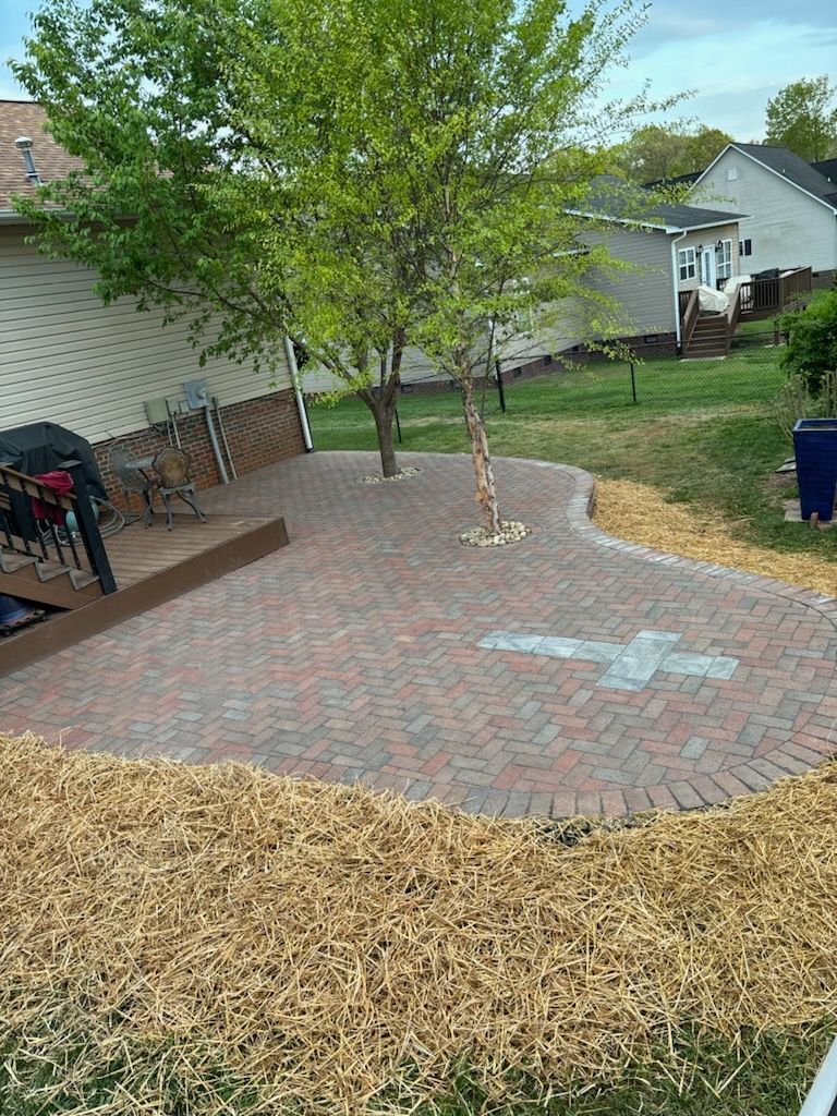 A brick patio with a cross painted on it is in the backyard of a house.