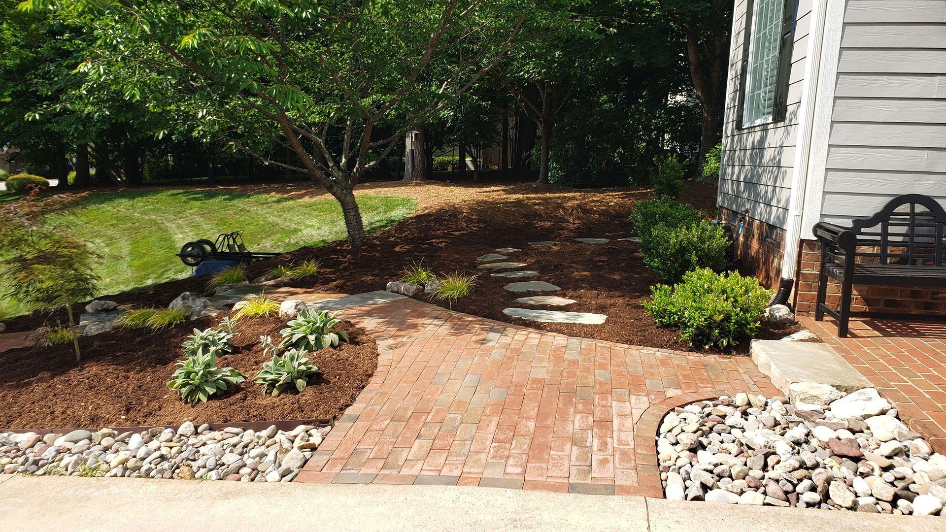 A brick walkway leading to a house with a bench in the background.