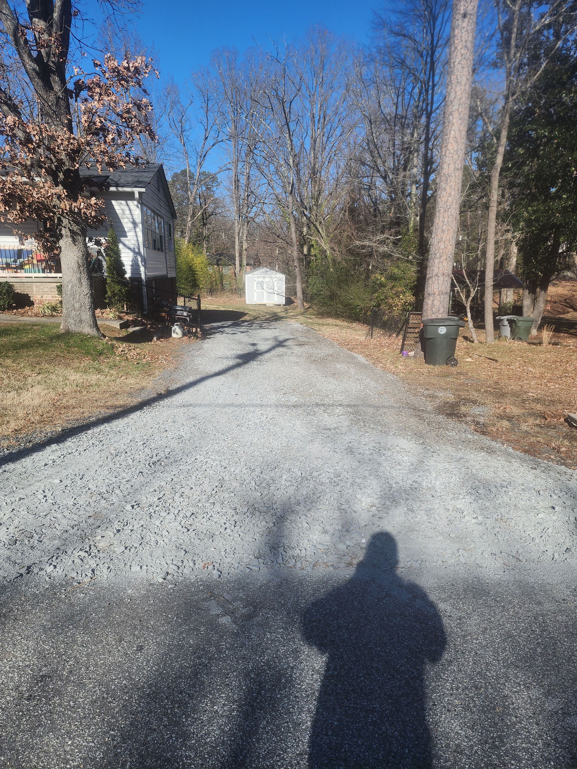A gravel driveway leading to a house with a shadow of a person on the ground.